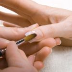 Professional manicurist applying liquid acrylic to nail extensio